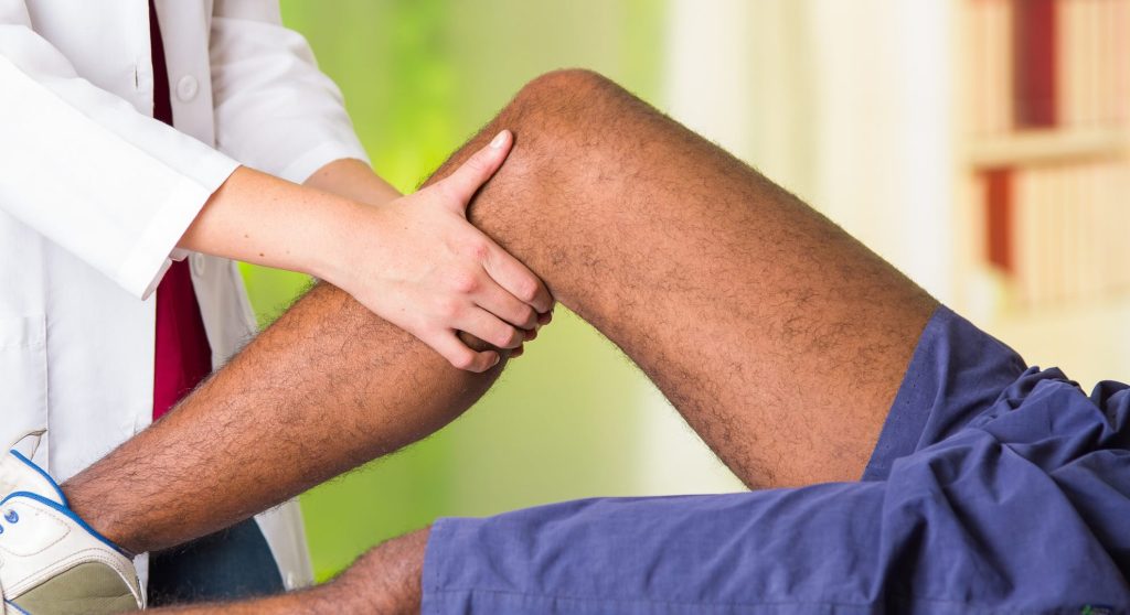 man getting knee treatment from physio therapist, her hands holding his leg and applying massage, injury medical concept