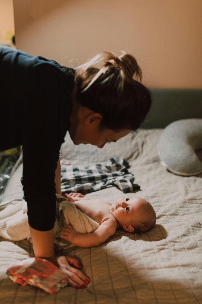 Mother lovingly interacts with her newborn baby on a cozy bed indoors.