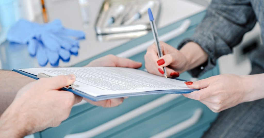 Patient signing healthcare agreement in doctor's office, focus on hands and document exchange.