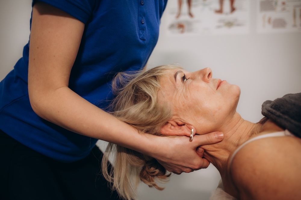 a rehabilitator massages the neck of an elderly woman